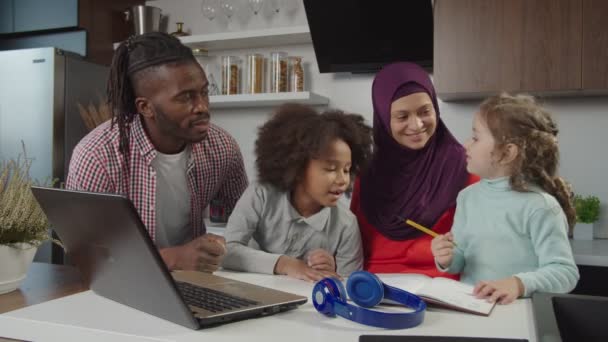 Glückliche multiethnische Eltern mit zwei niedlichen kleinen Mädchen, die Freizeit in der heimischen Küche genießen — Stockvideo