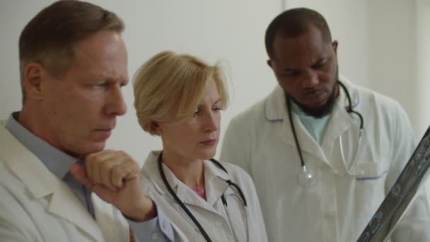 Retrato de médicos multiculturais perplexos preocupados examinando a ressonância magnética no consultório médico — Vídeo de Stock