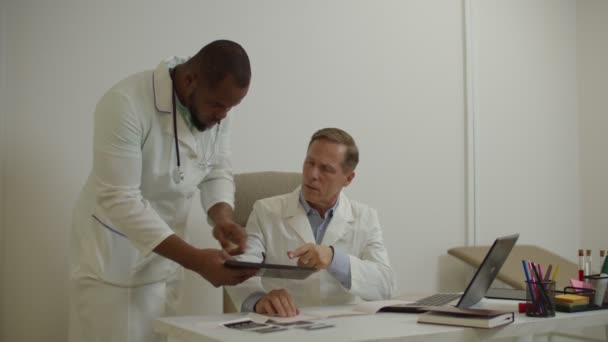 Afrikai amerikai orvos és tapasztalt férfi kolléga megvitatása orvosi vizsgálati jelentés tabletta pc — Stock videók