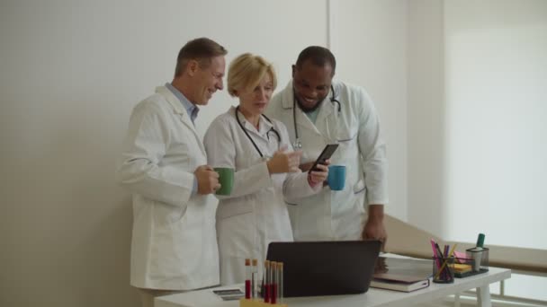 Positieve diverse multiraciale medisch personeel ontspannen na het werk en het delen van telefoon op medisch kantoor — Stockvideo