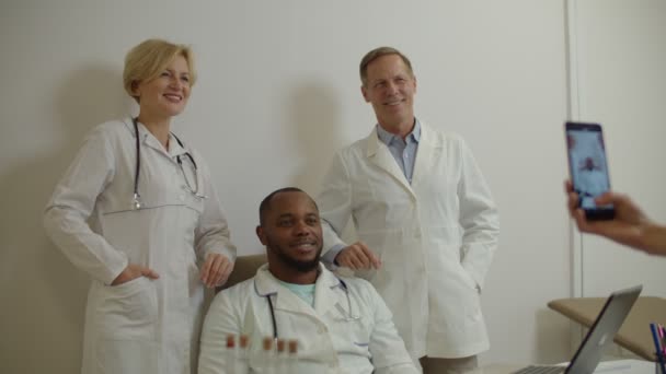 Pozitív soknemzetiségű egészségügyi dolgozók, akik a kórházi okostelefonra fotózott szelfihez pózolnak — Stock videók