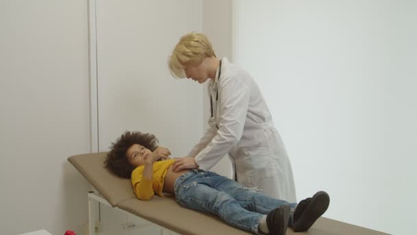 Opiekuńcza kobieta pediatra badania brzucha chorego wieku przedszkolnego wielorasowy chłopiec w gabinecie medycznym — Wideo stockowe