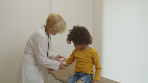 Ärztin bandagiert verletzten Arm einer entzückenden kleinen Patientin in Klinik — Stockvideo