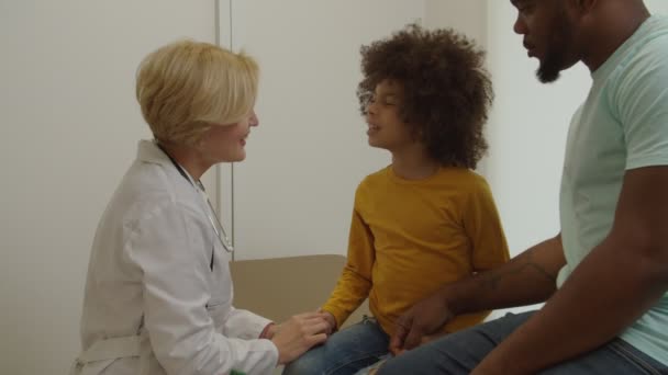 Pediatra bonita positivo que fala com pequeno paciente encantador durante o exame médico — Vídeo de Stock