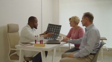 MRI taraması olan siyahi bir doktor hastanedeki orta yaşlı ve endişeli adama test sonuçlarını açıklıyor.