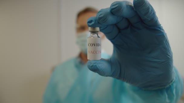 Primer plano de la mano del médico masculino en guantes médicos que sostienen la vacuna contra el coronavirus en interiores — Vídeos de Stock