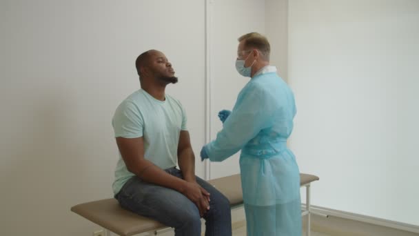Mannelijke arts in PBM die zwart patiëntenmonster neemt voor PCR-test op coronavirus in het ziekenhuis — Stockvideo