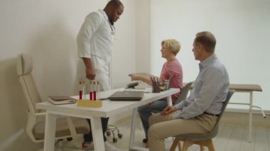 Afrikalı Amerikalı erkek doktor ofisteki orta yaşlı kadının kan basıncını ölçüyor.