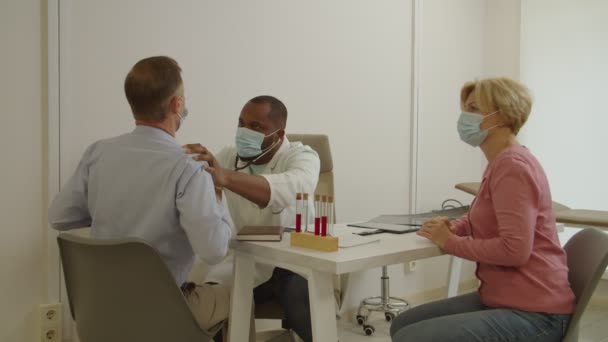 Afro-américain mâle médecin auscultant malade homme mature avec stéthoscope lors d'un examen médical — Video