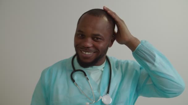 Muotokuva ystävällinen hymyilevä musta mies lääkäri stetoskooppi koskettaa päätä käsin sisätiloissa — kuvapankkivideo