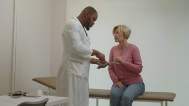 İlgilenen siyah doktor endişeli yetişkin kadın hastaya ultrason sonuçlarını açıklıyor.