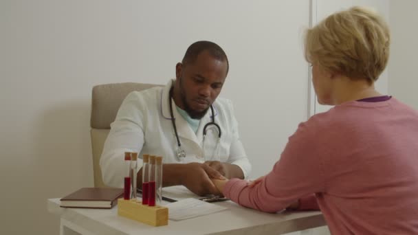 Африканский врач общей практики проверяет пульс у женщин среднего возраста, находящихся в офисе — стоковое видео