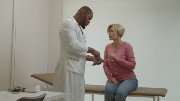 Pečující černý lékař vysvětlující výsledky ultrazvukového vyšetření ustaranému zralému pacientovi — Stock video