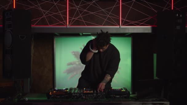 DJ afroamericano tocando set en vivo y mezclando música en la consola del tocadiscos en el escenario en el club nocturno — Vídeo de stock