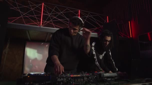 Energetyczne wieloetniczne męskie DJ-y w słuchawkach mieszające utwór muzyczny na mikserze dźwięku podczas występu — Wideo stockowe
