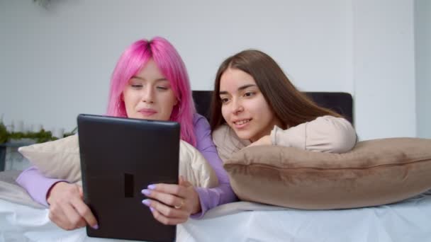 Retrato de adoráveis jovens mulheres deitadas na cama em rede no tablet digital — Vídeo de Stock