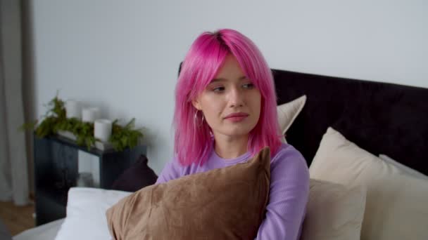 Deprimida mujer de pelo rosa bonita sentada en la cama con expresión molesta — Vídeos de Stock