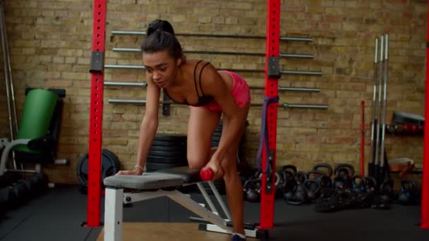 Atletisk aktiv pasform sort kvinde laver en-arm håndvægt række på bænken på gym – Stock-video