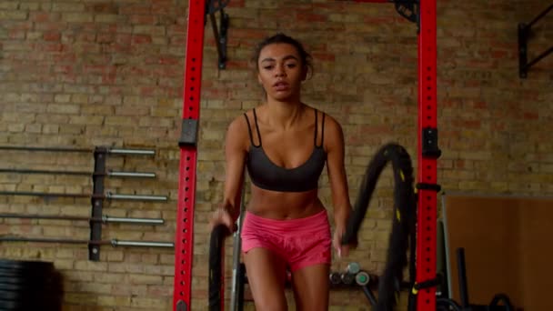 Mujer negra de fitness motivada haciendo entrenamiento cruzado con cuerdas de batalla en el gimnasio — Vídeos de Stock