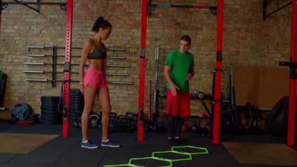 Fitness instructeur toont behendigheidsladder in en uit oefeningen voor vrouwelijke atleet — Stockvideo