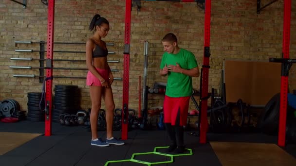 Fitness tränare visar sidan straddle hop motion till kvinna med hjälp av agility stege — Stockvideo