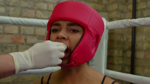 Zwarte vrouwelijke vechter in hoofddeksel inbrengen mondbeschermer met behulp van cutman — Stockvideo