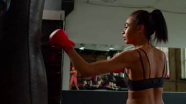 Yorgun Afrikalı Amerikalı bayan boksör dinleniyor ve kum torbasına yaslanıyor.