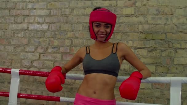 Портрет улыбающейся спортивной черной женщины-боксера, опирающейся на веревки внутри боксерского ринга — стоковое видео