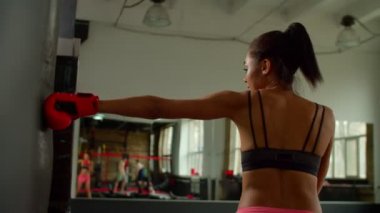 Kararlı sportif formda siyah kadın dövüşçü boks çantasıyla yumruk atıyor.