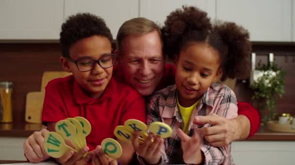 Cheerful granddad and smart African American grandchildren learning ABC indoors — Stockvideo