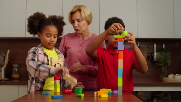 Sorglos multikulturelle Kinder und Großmutter spielen mit Spielzeugbausteinen — Stockvideo