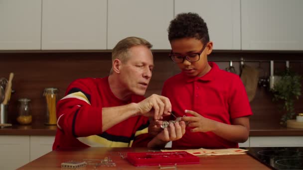 Opa und schulpflichtiger schwarzer Enkel bauen Spielzeug vom Metallbauer zusammen — Stockvideo