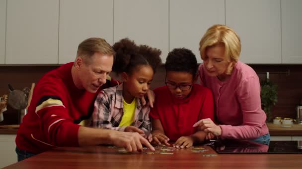 Positive grandparents with lovely multiracial children doing jigsaw puzzle — Vídeo de Stock