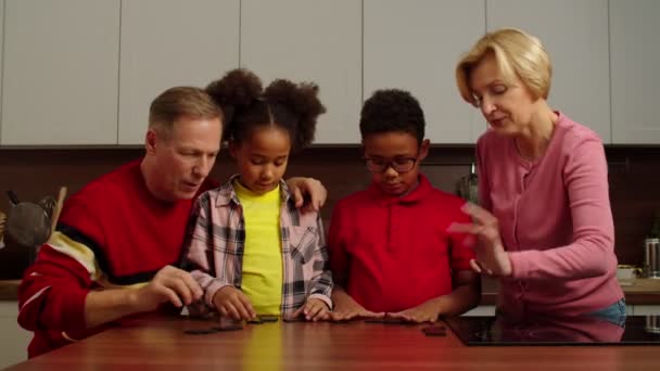 Loving grandparents teaching dominoes game to multiracial kids at home — Vídeo de Stock