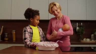 Neşeli ilköğretim çağı. Çok ırklı bir kız ve büyükannesi evde oyuncak bebekle oynuyor.