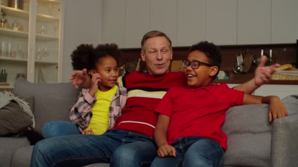 Happy grandpa with adorable school age multiracial kids bonding on sofa at home — Stockvideo