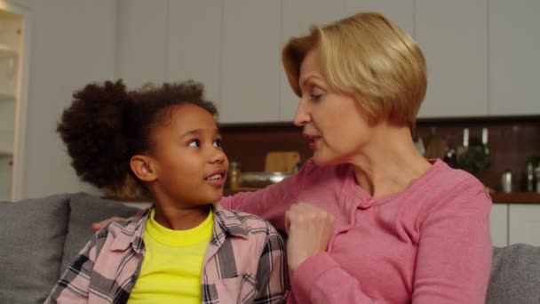Adorable school age multiracial girl and grandma whispering gossips at home — Stockvideo