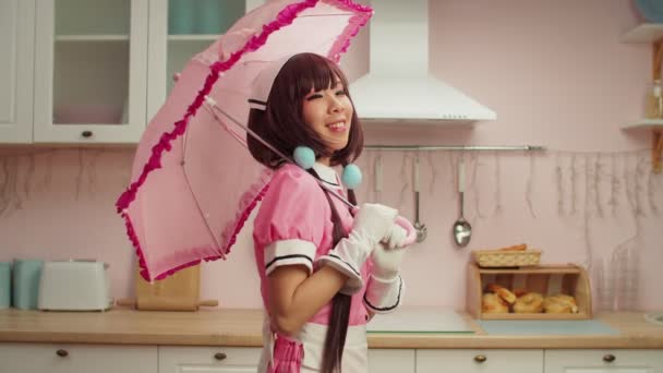 Lekfull charmig asiatisk kvinna i piga cosplay kostym poserar med rosa paraply — Stockvideo