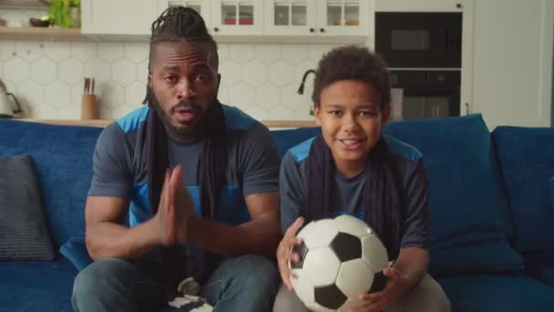 Afro-Amerikaanse vader en jongen kijken voetbal op tv, teleurgesteld door doel missen — Stockvideo