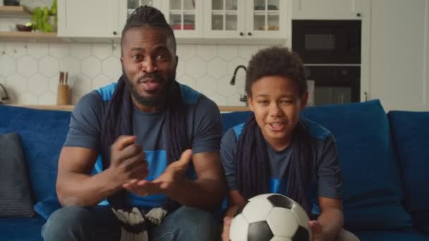 Vreugdevolle zwarte vader en zoon kijken naar voetbalwedstrijd op tv en het vieren van doel — Stockvideo