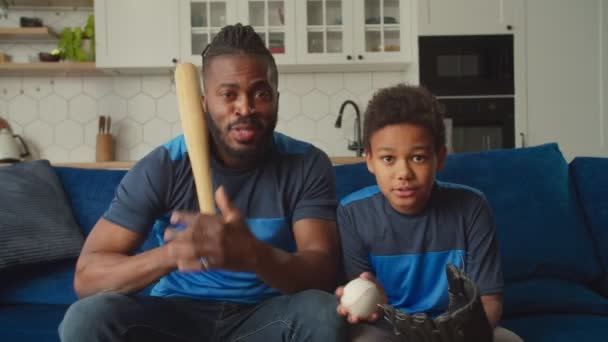 Alegre hijo afroamericano y padre viendo partido de béisbol en la televisión en casa — Vídeo de stock