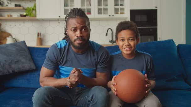 Svart pappa och son tittar på sport tv, besviken över nederlag för basketlag — Stockvideo