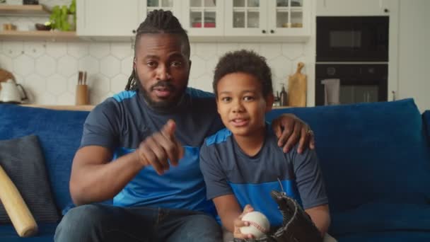 Pozytywna czarna rodzina z chłopcem oglądającym mecz baseballa w domu — Wideo stockowe