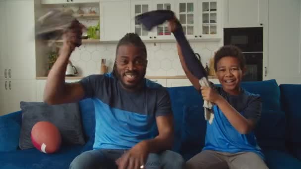 Emocionada familia negra de fanáticos del fútbol americano con bufandas animando equipo indoor — Vídeos de Stock