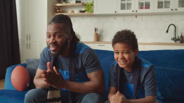 Família africana alegre de fãs de futebol americano assistindo jogo ao vivo na TV em casa — Vídeo de Stock