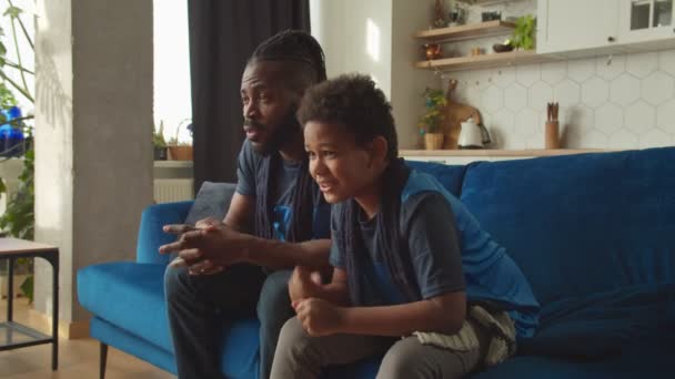 Hijo y papá afroamericanos viendo el partido de fútbol en la televisión, celebrando el gol — Vídeos de Stock