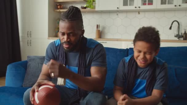 Black father and boy watching American football on tv, disappointed by team loss — Stock Video