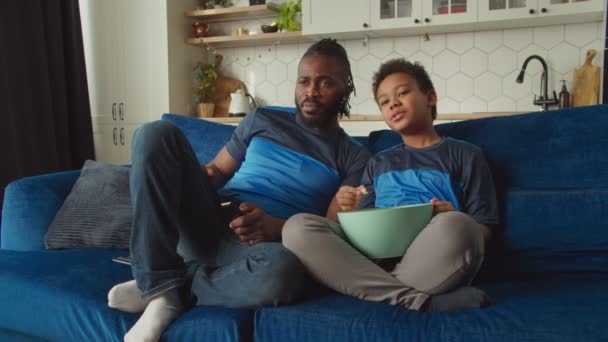 Relajados afroamericanos padre e hijo viendo la televisión y comiendo palomitas de maíz — Vídeos de Stock