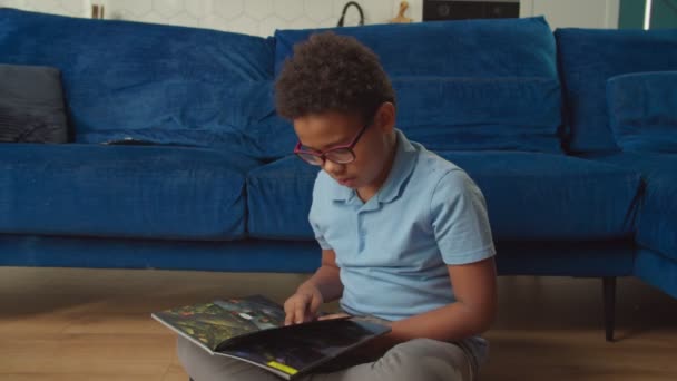 Veselý rozkošný školní věk černošky chlapec v brýlích čtení komiks uvnitř — Stock video