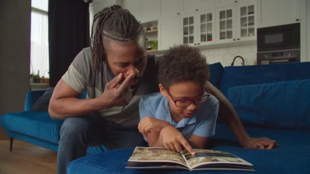 Amar al padre negro y al hijo en edad escolar compartiendo y discutiendo cómics en casa — Vídeos de Stock